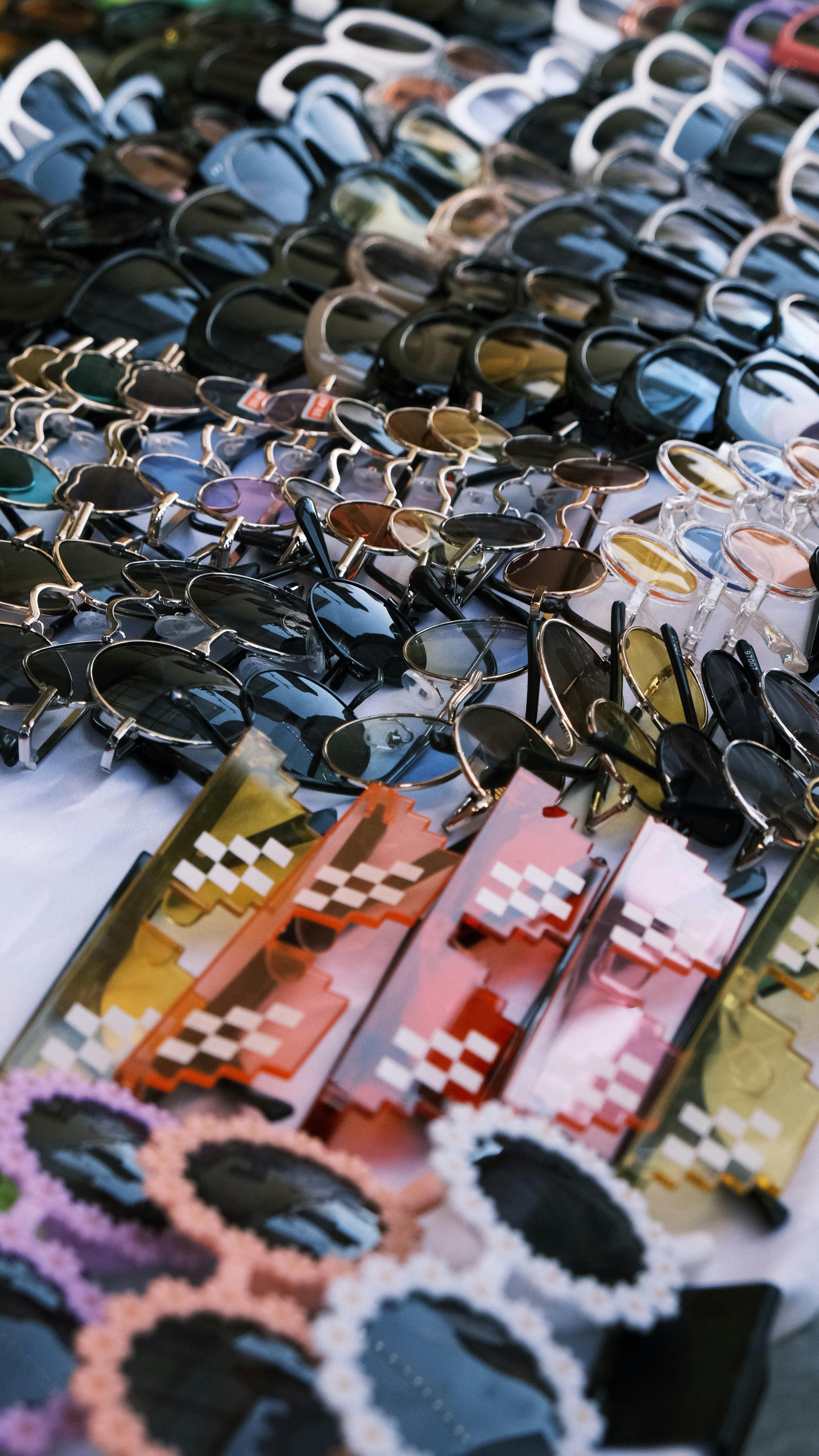 Five different colored sunglasses arranged in a row on a neutral background
